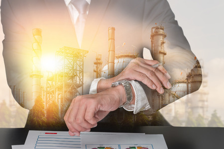 Double exposure of businessman look the watch, oil fuel, Electric generating factory, plant and sunset as business, appointment, industrial and energy concept.の写真素材