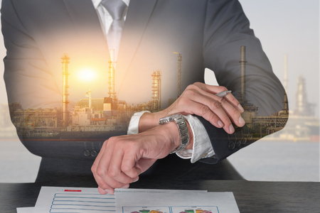 Double exposure of businessman look the watch, oil fuel, electric generating factory, plant near the river and sunset as business, appointment, industrial and energy concept.の写真素材
