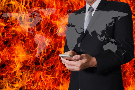 Double exposure of businessman hand hold smartphone, mobile and world map on fire blaze background as business, technology communication, urgent and rush concept.の写真素材