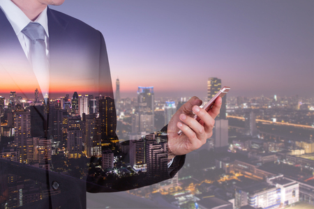 Double exposure of businessman use smartphone, communication networking telephone and cityscape urban in the night or twilight as business, technology, communication and telecom conceptの写真素材