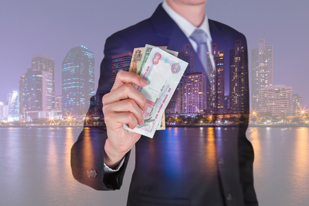 Double exposure of businessman hold United Arab Emirates Dirham (AED) money and night city as business, trade, investment and income conceptの写真素材