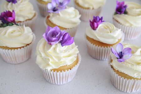 Edible purple freesia flowers on vanilla cupcakes with whipped cream frostingの写真素材