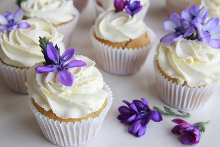 Homemade purple freesia flowers on vanilla cupcakes with whipped cream frostingの写真素材