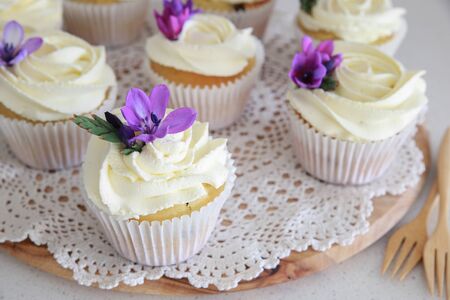 Homemade purple freesia flowers on vanilla cupcakes with whipped cream frostingの写真素材