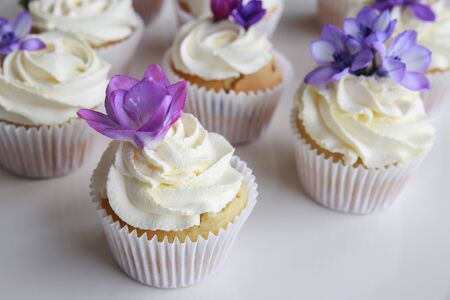 Homemade purple freesia flowers on vanilla cupcakes with whipped cream frosting