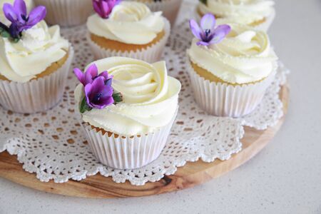Homemade purple freesia flowers on vanilla cupcakes with whipped cream frostingの写真素材