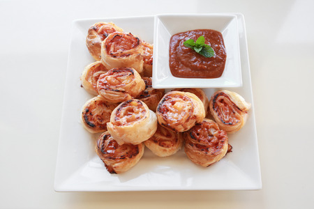 Homemade Hawaiian pizza rolls on white serving plate with tomato sauceの写真素材