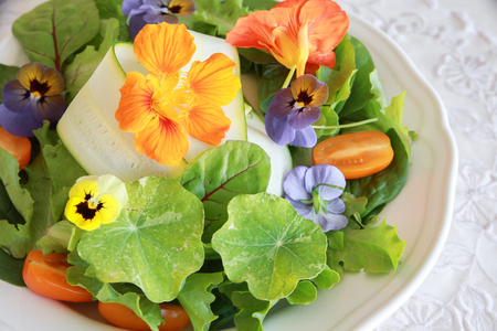 Fresh green salad with edible flowers in white serving dishの写真素材