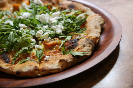 wood fired pumpkin feta rocket pizza on wooden plateの写真素材
