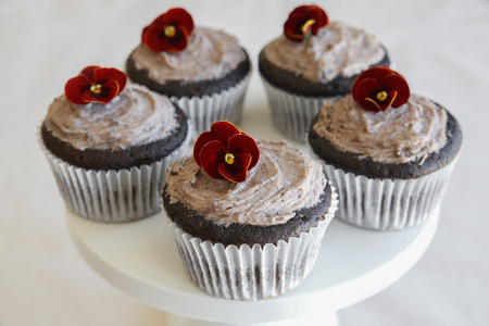 Homemade chocolate cupcakes with cookie and cream frosting and red edible flowersの写真素材