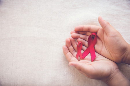 hands holding Red Ribbons on toning background, HIV/AIDS, Anosmia, Heart disease,Epidermolysis bullosa and Vasculitis awarenessの写真素材