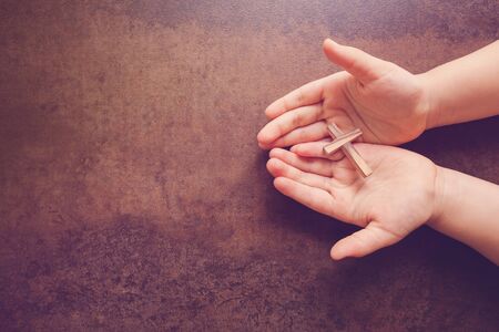Wooden cross on praying children hands, copy space dark toning backgroundの写真素材