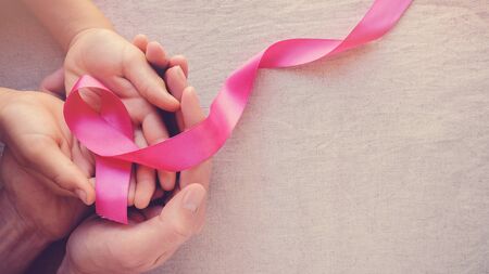 Adult and child hands holding pink ribbons, Breast cancer awareness, abdominal cancer awareness and October Pink panoramic backgroundの写真素材