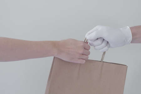 Hand with gloves giving eco paper bag, take away food, home delivery, donation conceptの写真素材