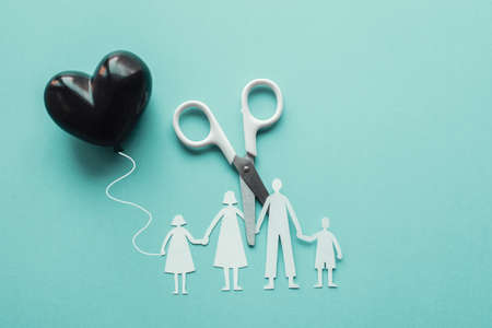 White scissor cutting family paper cut out holding black heart balloon on blue background, causes...
