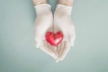 Doctor hands with medical gloves holding red heart, health insurance, donation, charity during covid-19 coronavirus pandemic, saving life, thank you and appreciation to doctorの写真素材