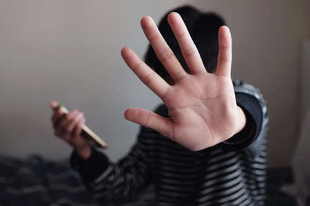 Young Asian preteen teenager boy holding a smartphone and showing a stop sign with his hand, Stop cyber bullying concept, mental health problemの写真素材