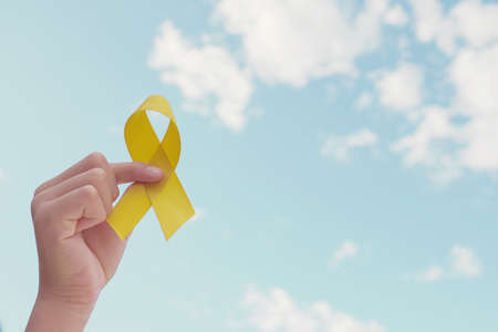 Hands holding yellow gold ribbon over blue skyの写真素材