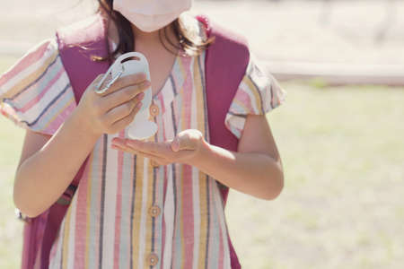 student girl wearing mask and holding hand sanitizer near playground