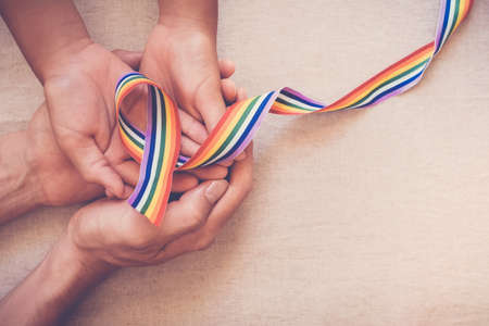 Hands holding gay pride rainbow ribbon for LGBT awarenessの写真素材