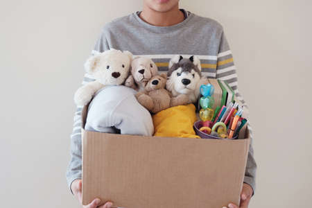 Young volunteer preteen teenage boy holding a box full of used toys, cloths, books and stationery for donationの写真素材