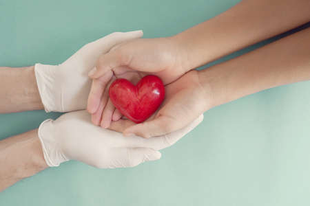 Doctor hands with medical gloves holding child hands and red heart, health insurance, donation, charity during covid-19 coronavirus pandemic, saving life, thank you and appreciation to doctorの写真素材