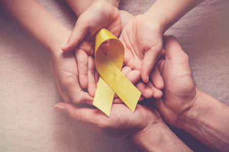 adult and children hands holding yellow gold ribbon, Sarcoma Awareness, Bone cancer, childhood cancer awarenessの写真素材