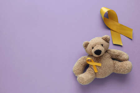 Children soft toy brown bear with yellow gold ribbons on purple background, Childhood cancer awarenessの写真素材