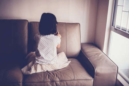 Lonely little girl playing by herself on sofa at home, Austism and child mental health conceptの写真素材