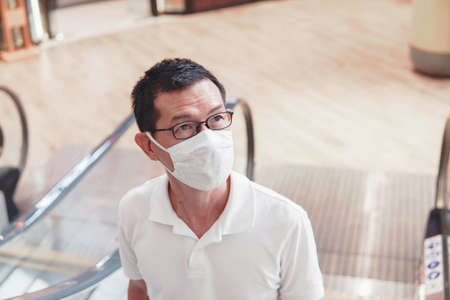 Middle aged Asian man wearing glasses and medical face mask on escalator,  Wuhan coronavirus outbreak, air pollution and health conceptの写真素材