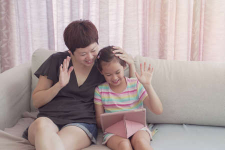 Mixed race young Asian girl and her mother making facetime video calling with laptop at home, using zoom learning online app, social distancing, isolation, homeschooling education, learning remotely conceptの写真素材