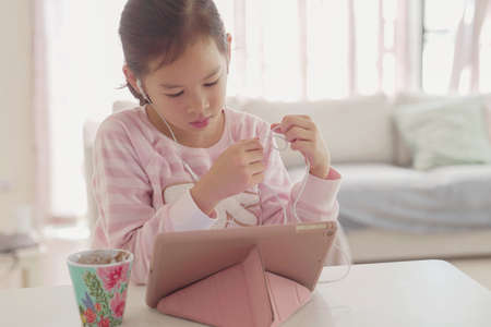mixed Asian girl using digital tablet at home, listening to podcast, gaming, online education,...
