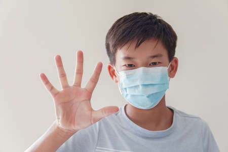Asian preteen boy wearing medical face mask and making stop sign, self-quarantine,  coronavirus, covid-19  virus outbreak epidemic pandemic, pm 2.5 air pollution and health conceptの写真素材