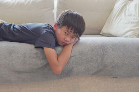Mixed race Asian preteen boy feeling bored lying on sofa at home, social distancing, quarantine, isolation concept, autism awareness, mental healthの写真素材