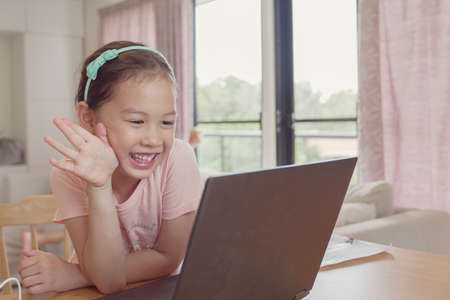 Mixed race young Asian girl making facetime video calling with laptop at home, using zoom learning...