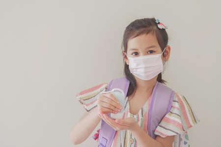 Mixed Asian girl wearing mask and applying hand sanitizer, school reopen, back to school after covid-19 coronavirus pandemic is over, new normal conceptの写真素材