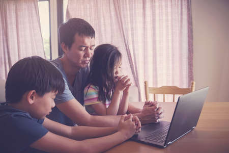 Children praying with father parent with laptop, family and kids worship online together at home, streaming online church service, social distancing conceptの写真素材