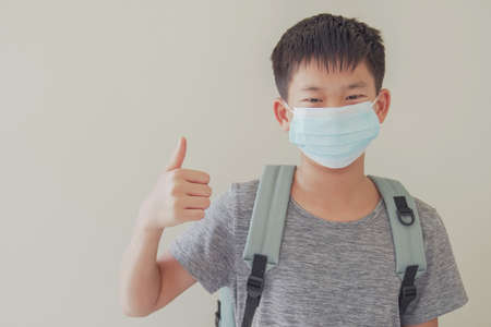 Asian preteen tween boy wearing mask and giving thumb up, school reopening, return back to school after covid-19 coronavirus pandemic is over, new normal conceptの写真素材