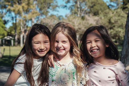 Happy and healthy mixed ethnic young little girls hugging and smiling in the park, best friends and...