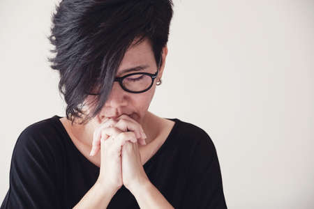 Asian middle aged woman wear glasses praying with hands together in the morning over white wallの写真素材