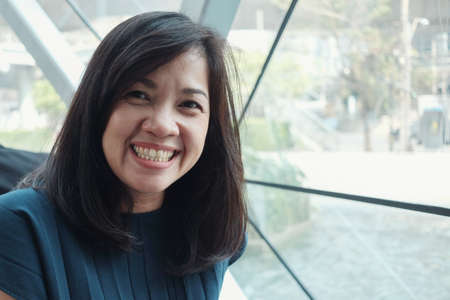 Headshot portrait of an Asian happy middle aged casual business working woman at coworking spaceの写真素材