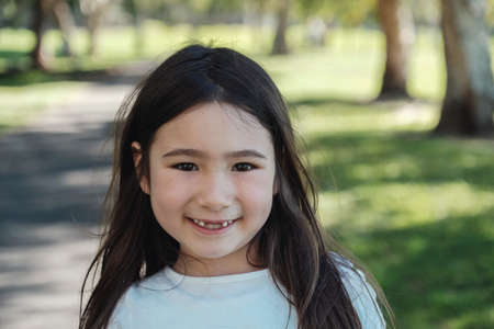 Happy mixed Asian girl missing her front milk teeth smiling with confident in the park, Child oral health and dental care conceptの写真素材
