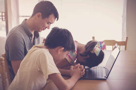 Children praying with father parent with laptop, family and kids worship online together at home, streaming church service, social distancing conceptの写真素材