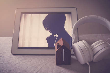 Mixed Asian woman praying with digital tablet, worship online at home, streaming online church service, social distancing, new normal conceptの写真素材