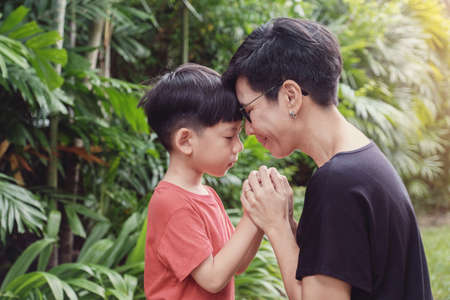 Young Asian boy praying with his mother in the park outdoors, family prayの写真素材
