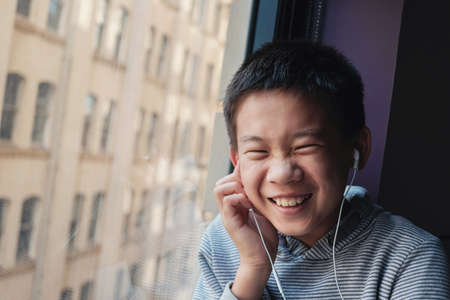 Happy Asian preteen boy using digital tablet at home, listening to podcast, gaming, online...