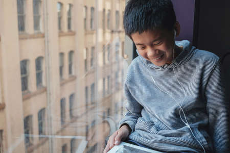 Young  mixed Asian preteen boy using digital tablet at home, listening to podcast, gaming, online...