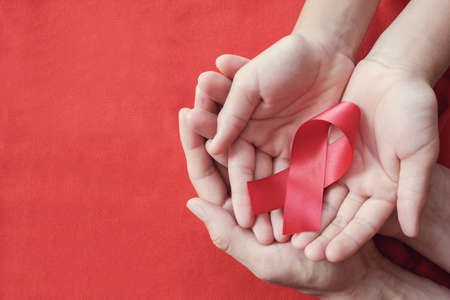 Hands holding red ribbon on red background, hiv awareness concept, world AIDS day, world hypertension dayの写真素材