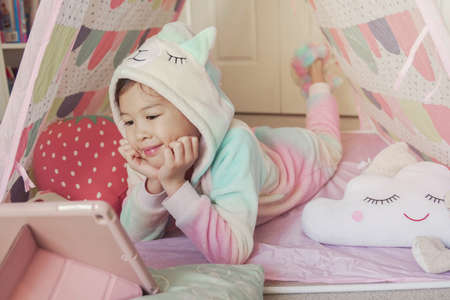 Mixed race Asian girl making facetime video calling with tablet at home, using zoom learning online app, social distancing, isolation, homeschooling education, learning remotely conceptの写真素材