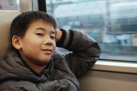 Portrait of tween mixed Asian boy in public train, preteen travel tourist on vacation in Japan winterの写真素材